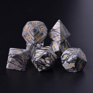 以下が含まれることがあります： さまざまな形状の7つの多面体サイコロのセット。d4、d6、d8、d10、d12、d20、およびパーセンタイルサイコロが含まれます。サイコロはグレーで、黒い縞模様と金色の数字が付いています。テーブルゲームに最適です。