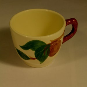 Puede incluir: Una taza de cerámica blanca con asa marrón y un diseño de manzana verde y marrón.
