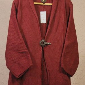 May include: A burgundy waffle knit cardigan with a shawl collar and a single button closure. The cardigan has long sleeves and a relaxed fit.