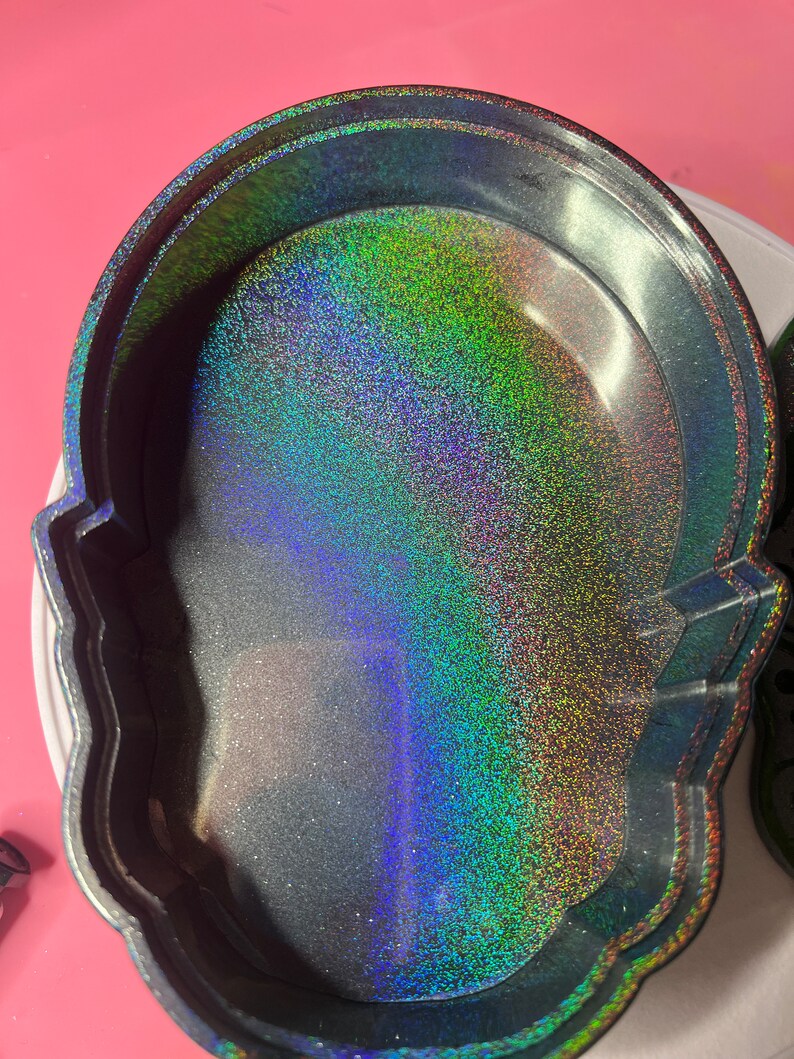 K&ouml;nnte beinhalten: Eine schwarze Sch&auml;del-Schmuckschatulle mit glitzerndem, irisierendem Innenraum. Der Glitter ist eine Mischung aus Gr&uuml;n, Blau und Lila.