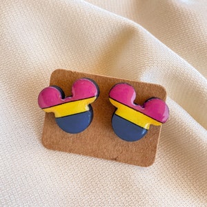 Puede incluir: Un par de pendientes de madera con forma de Mickey Mouse. Los pendientes están pintados en tonos de rosa, amarillo y azul.