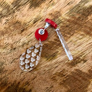 May include: Red and clear acrylic dangle earrings with a Mickey Mouse head pattern. The earrings have a red post and a clear acrylic dangle with a Mickey Mouse head pattern.