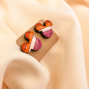 May include: A pair of colorful striped Mickey Mouse-shaped earrings on a brown card.