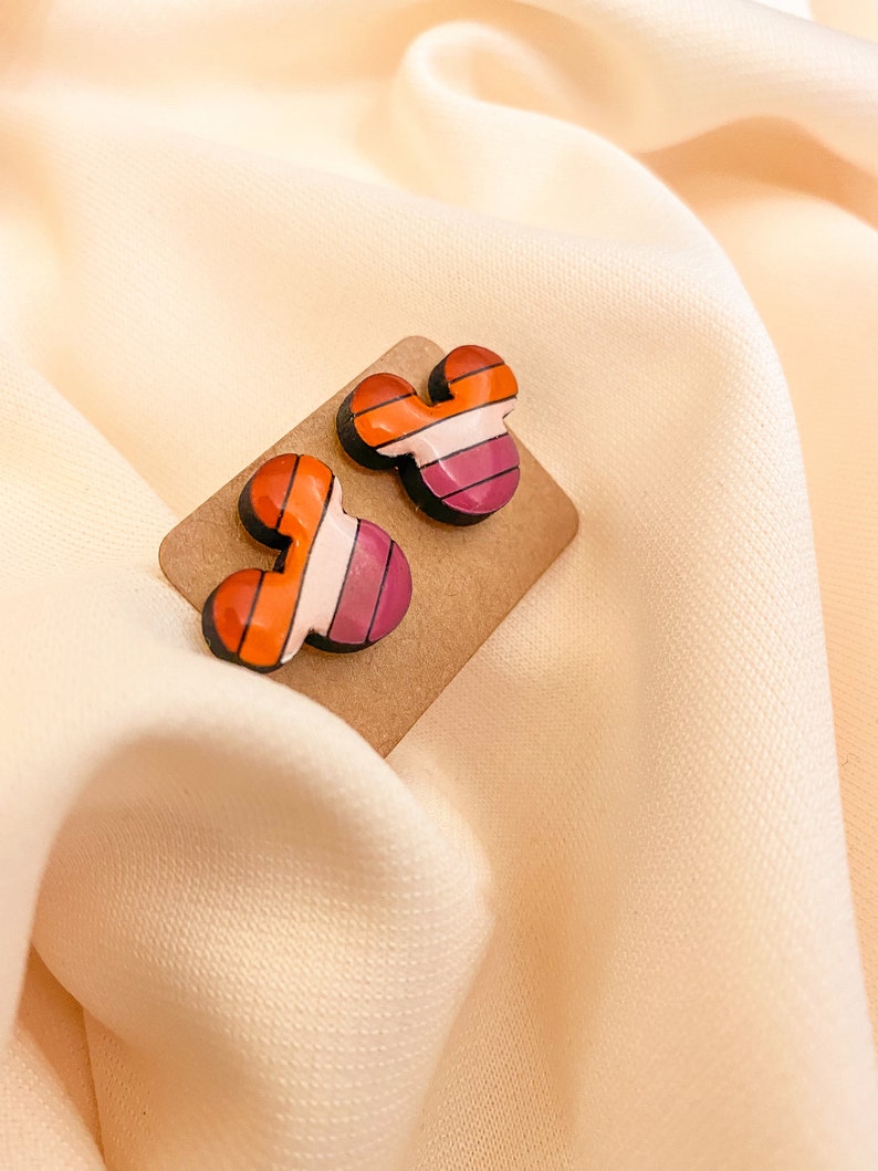 May include: A pair of colorful striped Mickey Mouse-shaped earrings on a brown card.