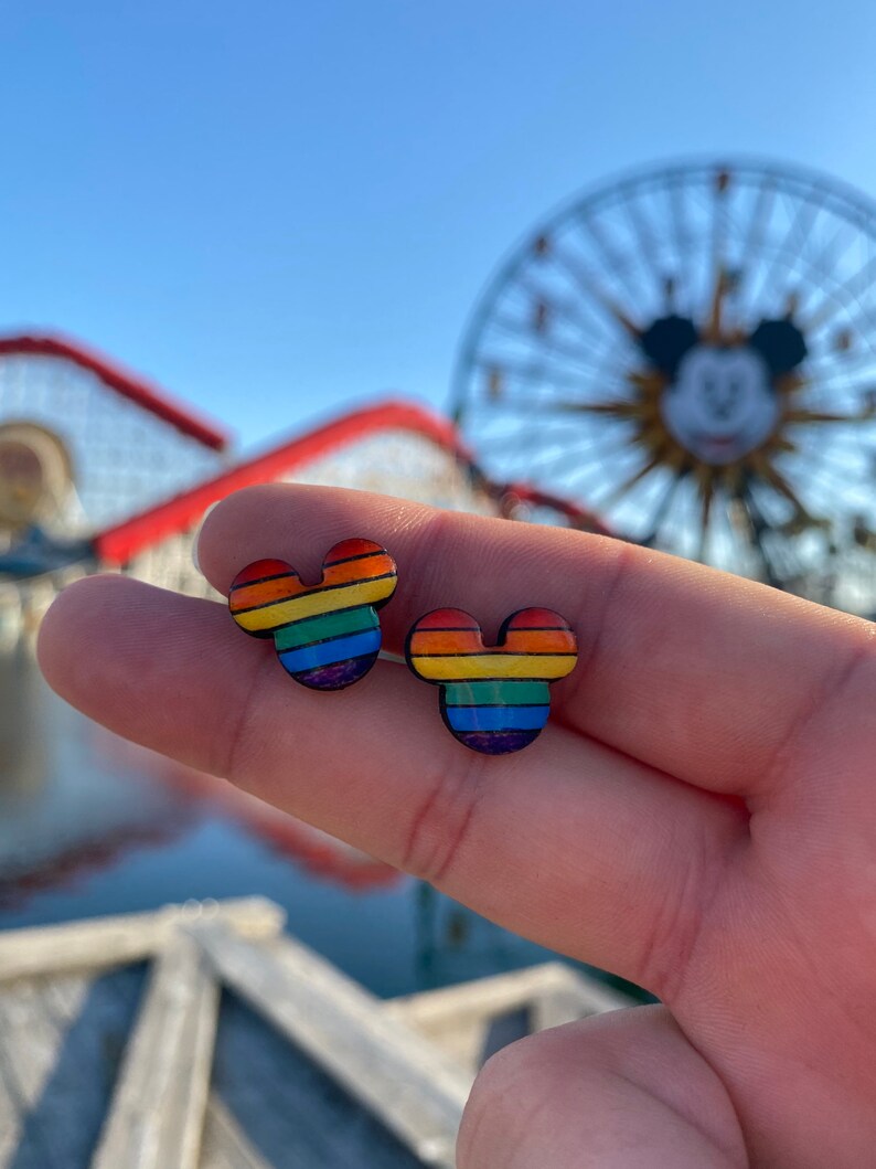 May include: A pair of rainbow-colored Mickey Mouse-shaped earrings. The earrings are made of wood and have a rainbow stripe pattern.