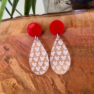 May include: A pair of red and clear dangle earrings. The clear teardrop-shaped earrings feature a white Mickey Mouse head pattern.
