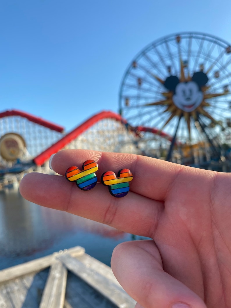 May include: A pair of rainbow Mickey Mouse-shaped earrings. The earrings are made of a colorful material and have a black outline.