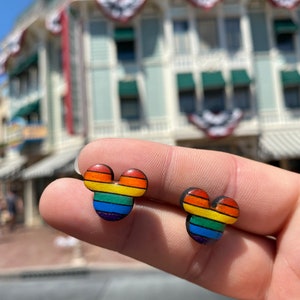 May include: A pair of rainbow Mickey Mouse-shaped earrings. The earrings are made of wood and have a rainbow stripe design.