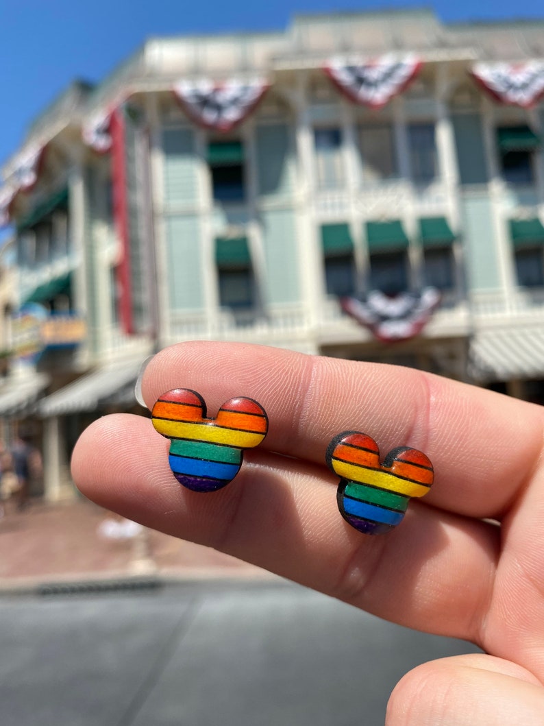 May include: A pair of rainbow Mickey Mouse-shaped earrings. The earrings are made of wood and have a rainbow stripe design.
