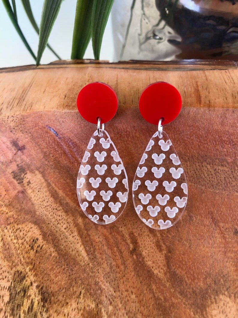 May include: A pair of red and clear acrylic earrings with a Mickey Mouse pattern. The earrings are teardrop shaped and have a red circle at the top.