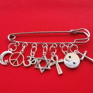 Broche KILT PIN con dijes en tono plateado COEXIST para representar a todas las personas que viven juntas en paz y armonía, asegurado con un cierre de langosta.