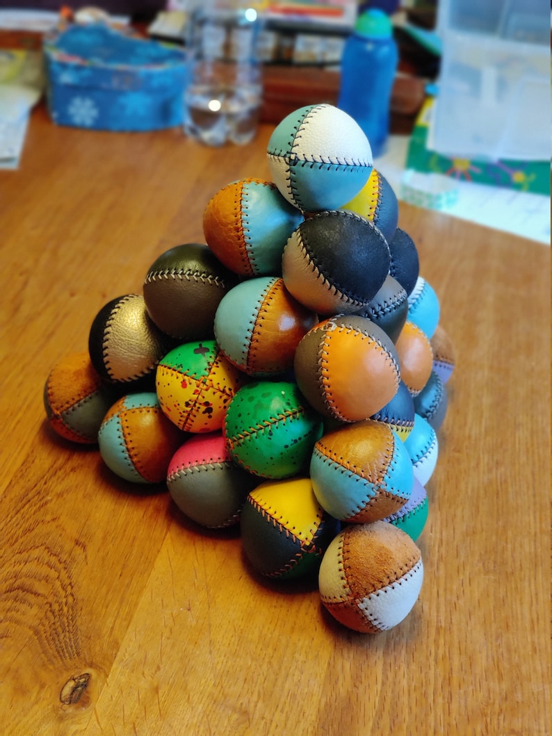 May include: A pyramid of colorful leather juggling balls. The balls are made of different colors and patterns, including blue, green, brown, yellow, and pink.