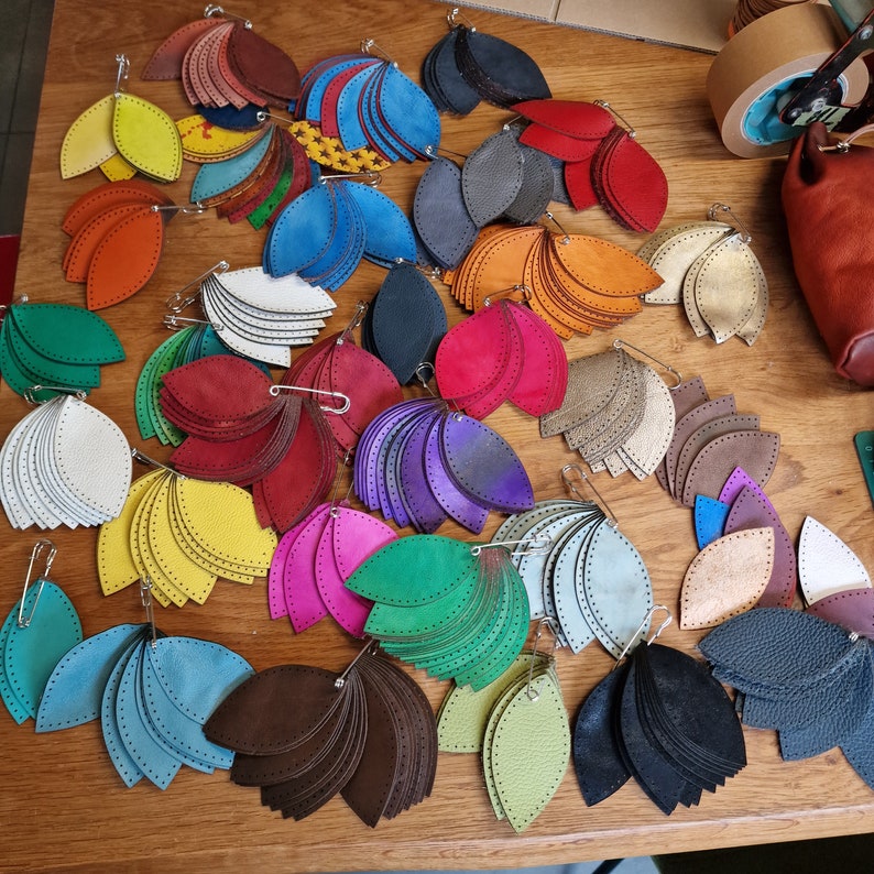 May include: A collection of colorful leather leaves with decorative stitching. The leaves are arranged in a variety of shapes and sizes, and some have safety pins attached.