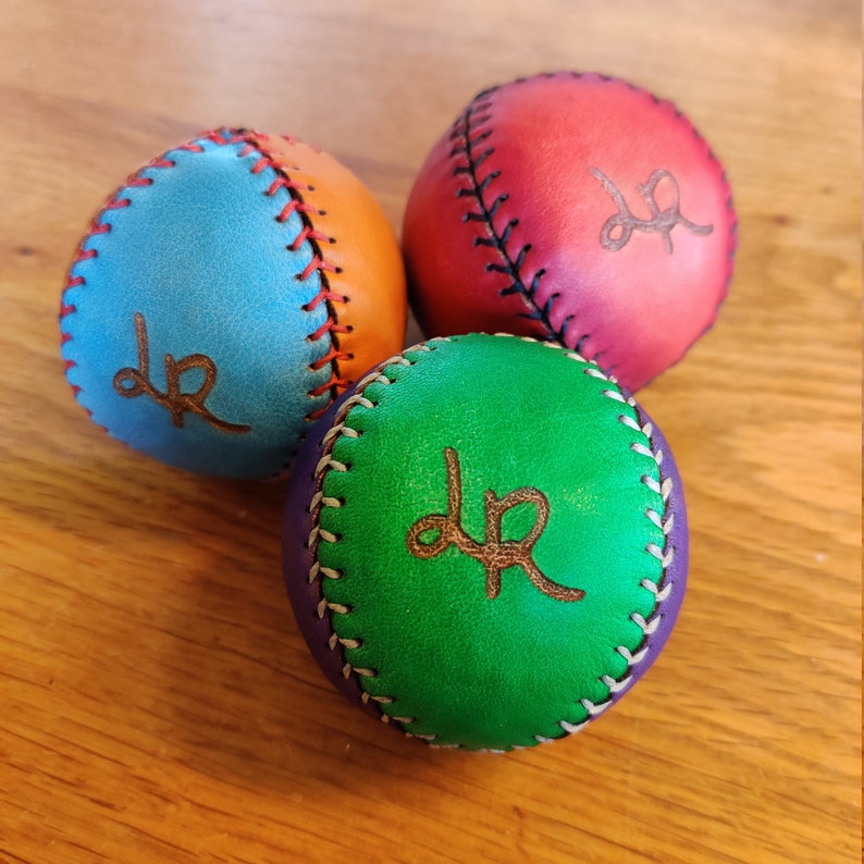 May include: Three leather baseballs, each a different color: blue, red, and green. Each ball has white stitching and the letters "dr" are embossed on the surface.