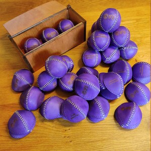May include: A wooden box with a purple leather ball inside. The box is labeled "IFS Talent Management". There are many purple leather balls with the IFS logo on them scattered on a wooden table.