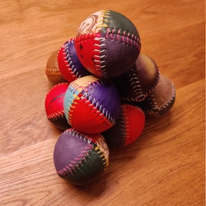 May include: A stack of eight colorful leather balls with stitched seams. The balls are arranged in a pyramid shape and have a variety of patterns and colors, including red, blue, green, and yellow.