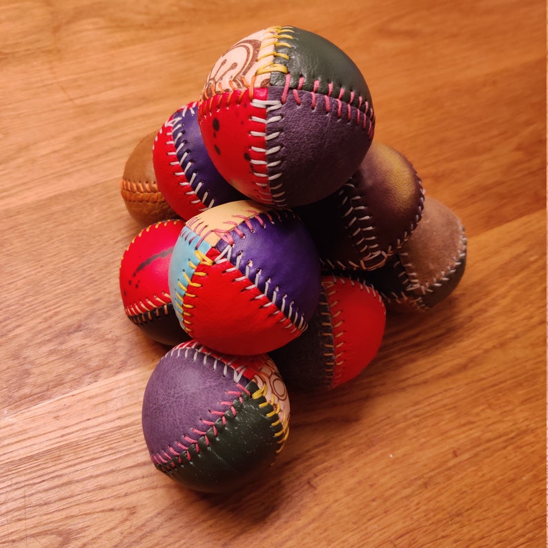 May include: A stack of eight colorful leather balls with stitched seams. The balls are arranged in a pyramid shape and have a variety of patterns and colors, including red, blue, green, and yellow.