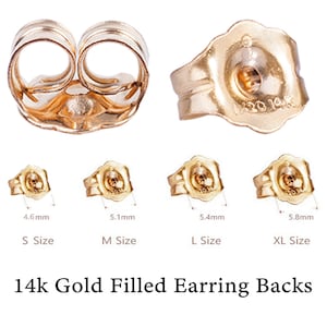 Puede incluir: Cuatro tamaños de respaldos de pendientes de oro de 14 quilates. Los respaldos se muestran en primer plano. Los tamaños están etiquetados como S, M, L y XL. Las medidas son 4,6 mm, 5,1 mm, 5,4 mm y 5,8 mm.