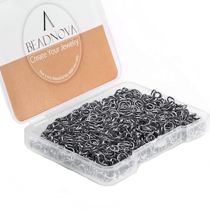Op de afbeelding: Een doorzichtige plastic doos gevuld met kleine, zilverkleurige sprongringen. Het deksel van de container is open en onthult de inhoud. De container heeft een label met de tekst "BEADNOVA Create Your Jewelry".