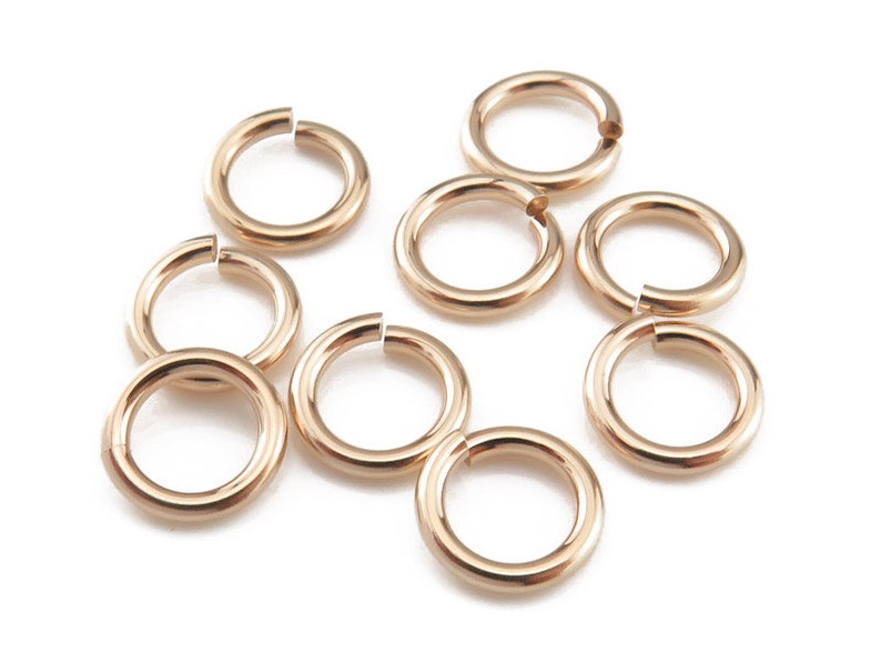 May include: A set of ten gold-toned jump rings. The rings are all the same size and are arranged in a random pattern.