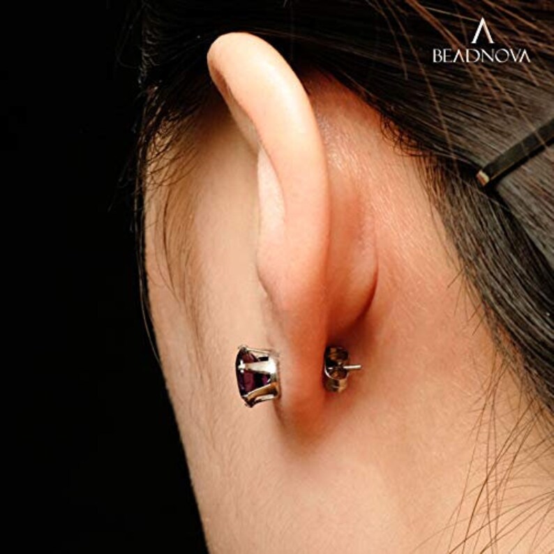 Puede incluir: Primer plano de una oreja con un peque&ntilde;o pendiente de piedra preciosa p&uacute;rpura. El pendiente es de plata y tiene un dise&ntilde;o sencillo.
