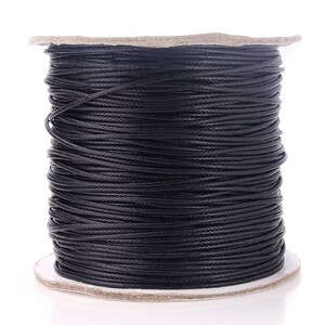 May include: A spool of black waxed cotton cord. The cord is wound tightly around a cardboard spool.