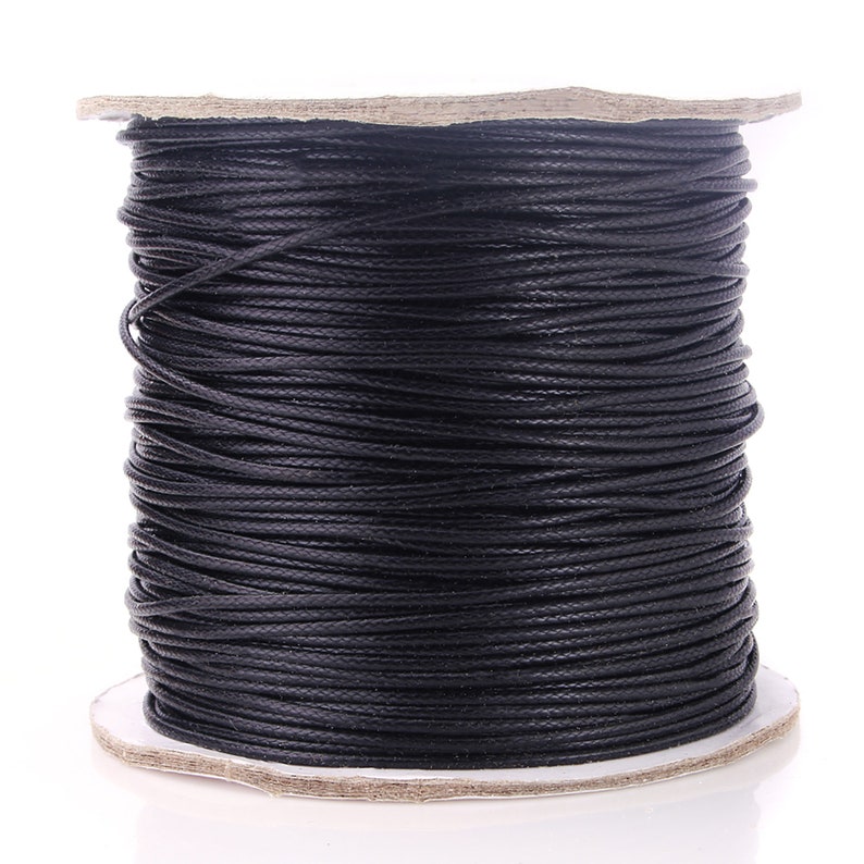 May include: A spool of black waxed cotton cord. The cord is wound tightly around a cardboard spool.