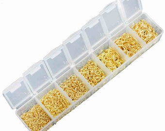 May include: A clear plastic storage box with six compartments filled with gold jump rings of various sizes.