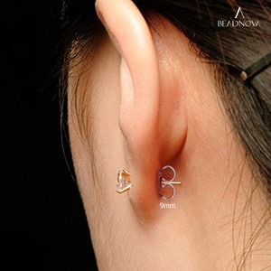 May include: A close-up of a gold earring with a clear cubic zirconia stone. The earring is 9mm in diameter and has a butterfly back.
