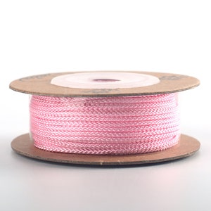 Puede incluir: Una bobina de cord&oacute;n rosa envuelta alrededor de una bobina de cart&oacute;n marr&oacute;n.