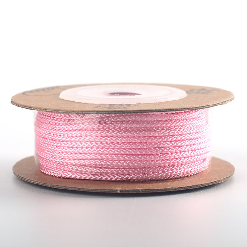 Puede incluir: Una bobina de cord&oacute;n rosa envuelta alrededor de una bobina de cart&oacute;n marr&oacute;n.