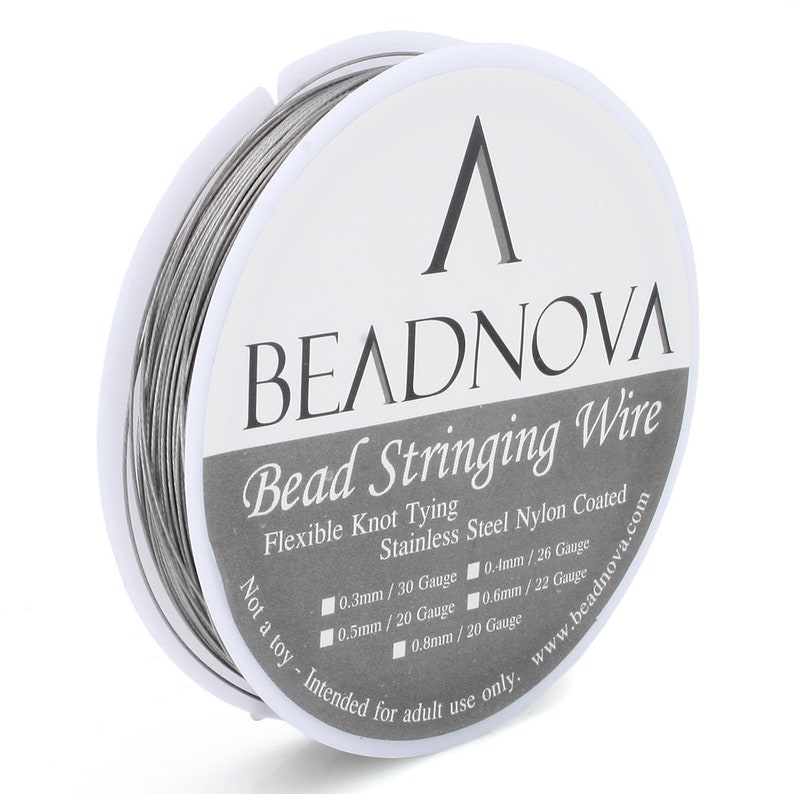 Puede incluir: Un carrete de hilo plateado para enhebrar cuentas con una etiqueta blanca que dice "BEADNOVA Bead Stringing Wire Flexible Knot Tying Stainless Steel Nylon Coated Not a toy - Intended for adult use only. www.beadnova.com 0.3mm / 30 Gauge 0.4mm / 26 Gauge 0.5mm / 20 Gauge 0.6mm / 22 Gauge 0.8mm / 20 Gauge"