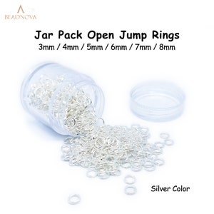 Könnte beinhalten: Ein Glas mit silbernen offenen Sprungringen in verschiedenen Größen, darunter 3 mm, 4 mm, 5 mm, 6 mm, 7 mm und 8 mm. Das Glas ist offen und einige Ringe fallen heraus.