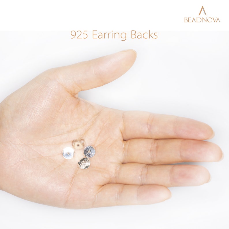 May include: A close-up of a hand holding four silver earring backs. The earring backs are small and round, with a small hole in the center. The text "925 Earring Backs" is visible in the image.