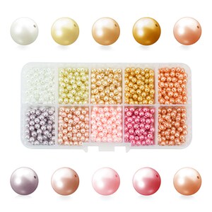 May include: A clear plastic organizer filled with various colors of faux pearls. The pearls range in size and color, including white, gold, bronze, and pink. The top row features larger pearls, while the rest of the organizer contains smaller beads.