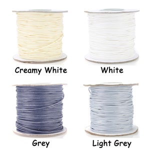 May include: Four spools of cord in different colors: creamy white, white, gray, and light gray. The spools are all the same size and are arranged in a grid pattern.