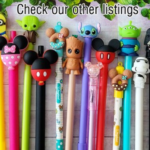 May include: A collection of 13 colorful pens with various character toppers, including Mickey Mouse, Yoda, a donut, and a Stormtrooper.  The pens are arranged on a white wooden surface.  Check our other listings.