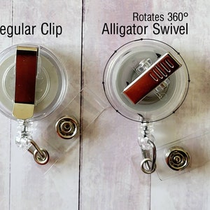 May include: Two clear retractable badge holders with different clips. The left holder has a regular clip. The right holder has a swivel alligator clip that rotates 360 degrees. Both holders have a clear plastic body and a silver metal clip.