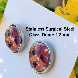 Puede incluir: Pendientes de bot&oacute;n de acero inoxidable con c&uacute;pula de cristal. Los pendientes presentan un dise&ntilde;o floral con tonos rojos, naranjas y negros. El texto de la imagen dice "Stainless Surgical Steel Glass Dome 12 mm."