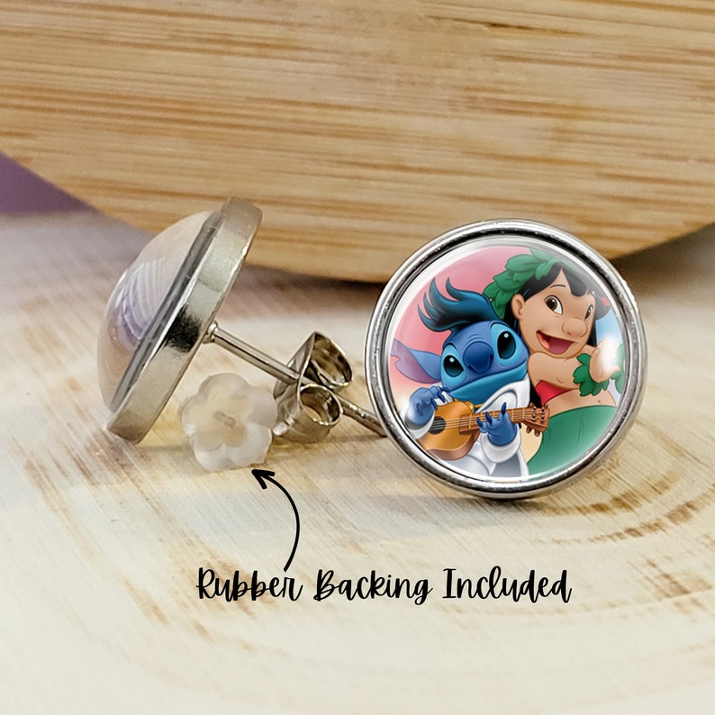 Puede incluir: Un par de pendientes de bot&oacute;n redondos con un engaste de metal plateado. Un pendiente presenta una imagen de dibujos animados de Stitch y Lilo. El otro pendiente tiene un dise&ntilde;o transparente y abovedado. El texto "Rubber Backing Included" es visible.