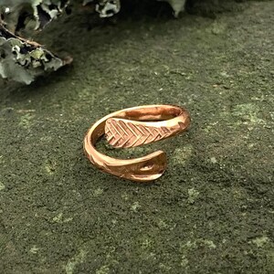 May include: A rose gold ring with a textured leaf design. The ring is open and adjustable.