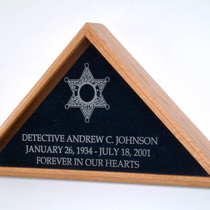 May include: A wooden shadow box with a black velvet interior. The box features a silver star with a circle in the center and the text "DETECTIVE ANDREW C. JOHNSON JANUARY 26, 1934 - JULY 18, 2001 FOREVER IN OUR HEARTS".