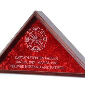 May include: A wooden triangle-shaped shadow box with a red velvet interior. The box features a white engraved firefighter emblem with the words "FIRE" and "RESCUE". The box also includes a personalized inscription: "CAPTAIN STEPHEN FALLEN JUNE 27, 1917 - MAY 08, 1988 BELOVED HUSBAND AND FATHER"