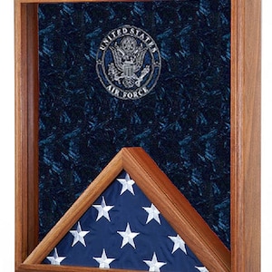 May include: A wooden shadow box with a blue velvet background and a silver United States Air Force emblem. A folded American flag is displayed in the lower right corner of the box.