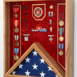 May include: A wooden shadow box with a red velvet interior displays a collection of military medals, ribbons, and insignia. A folded American flag is displayed in the lower portion of the box.