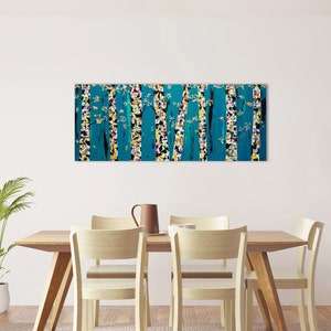 May include: A teal abstract painting of trees with white and yellow accents hangs above a wooden dining table with four chairs. The table is set with a brown pitcher and a white cup.