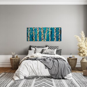 May include: A bedroom interior with a white bed, a gray throw blanket, and a large abstract painting of trees in shades of blue, yellow, and white hanging above the bed.