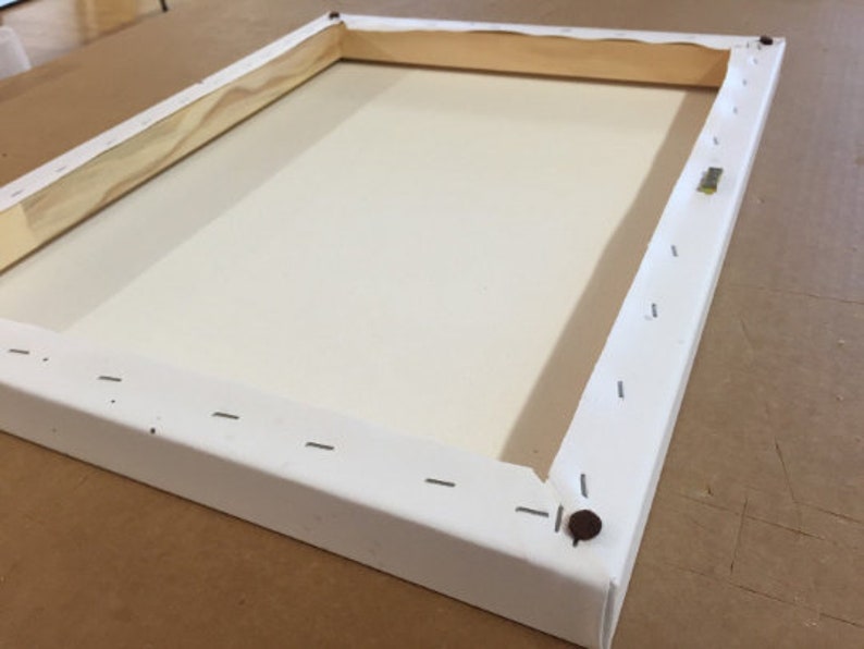 May include: White canvas stretched over a wooden frame with staples securing the canvas to the frame. The frame is made of wood and has a white finish.