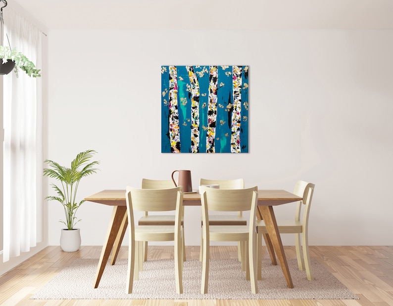 May include: Abstract painting of birch trees with white bark and colorful accents against a teal blue background. The painting is framed and hanging on a white wall above a wooden dining table with four chairs.