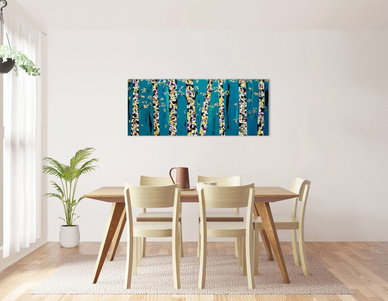 May include: A teal abstract painting of trees with white and yellow accents hangs above a wooden dining table with four chairs. The table is set with a brown pitcher and a white cup.